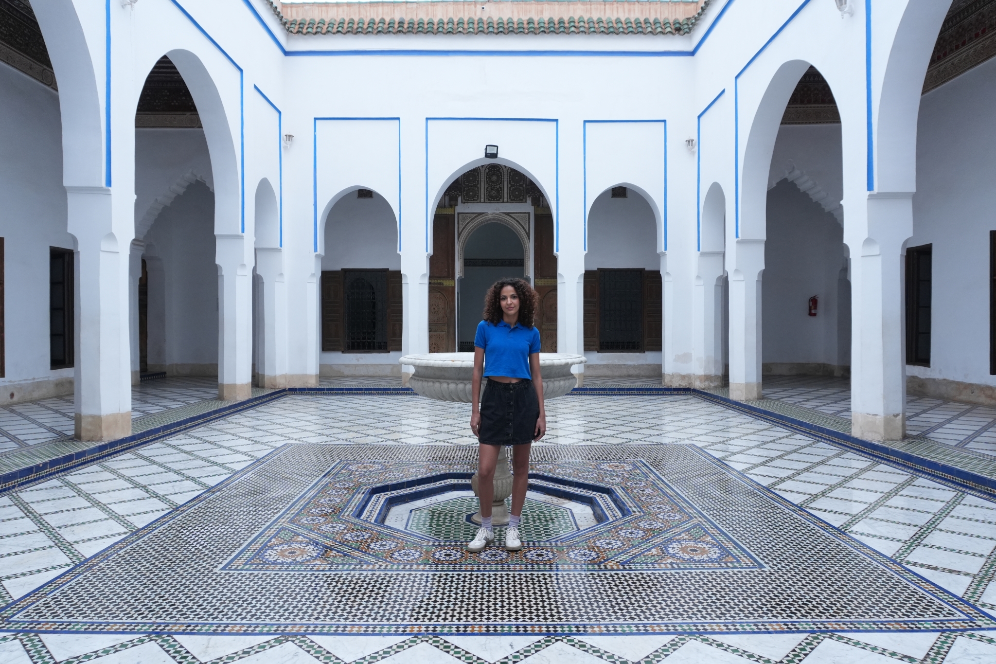Sample image of a woman standing at the centre of a courtyard in a building, taken with a focal length of 16mm