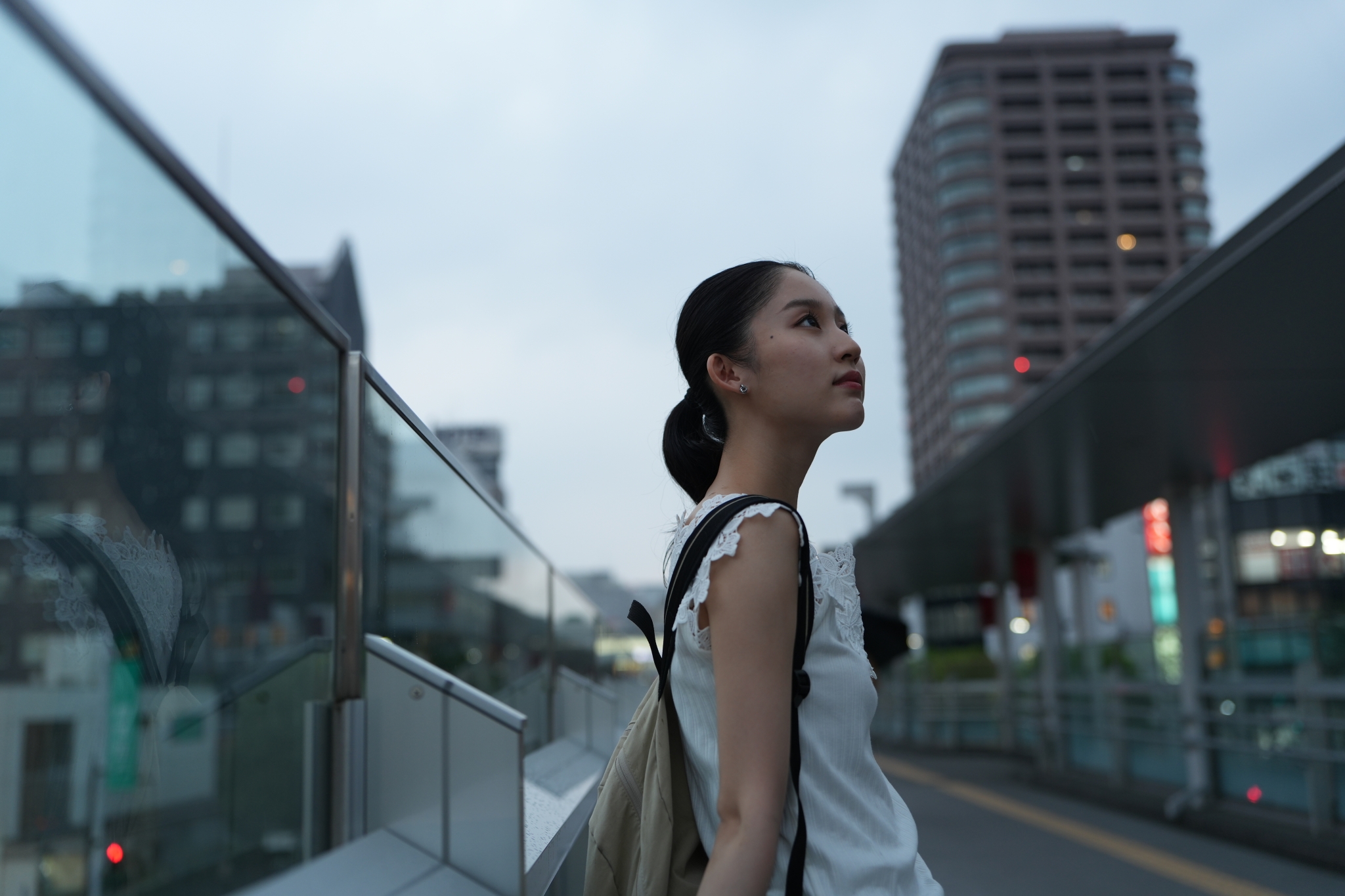 A woman gazing into the distance, with tall buildings rising in the background Click to open modal