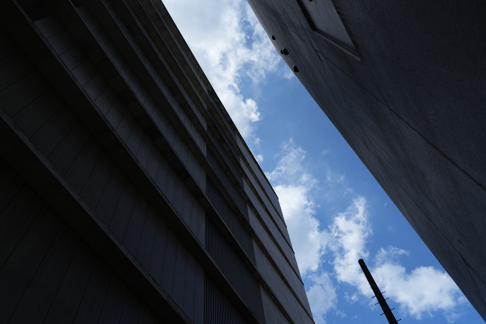 Photographed from below between two buildings, with a blue sky and white clouds in the center. The chromatic aberration is suppressed in the edge of the buildings Click to open modal