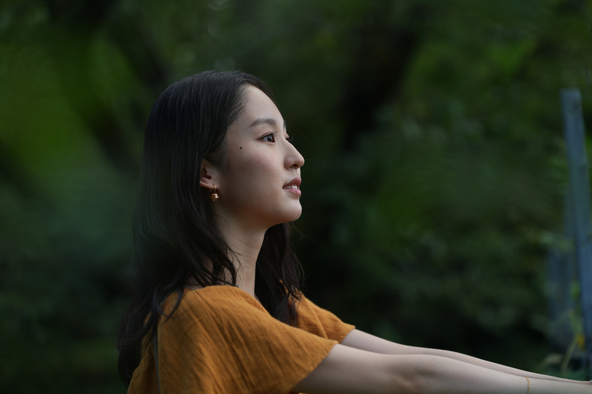 A woman wearing an orange top is gazing into the distance while turning to the side Click to open modal