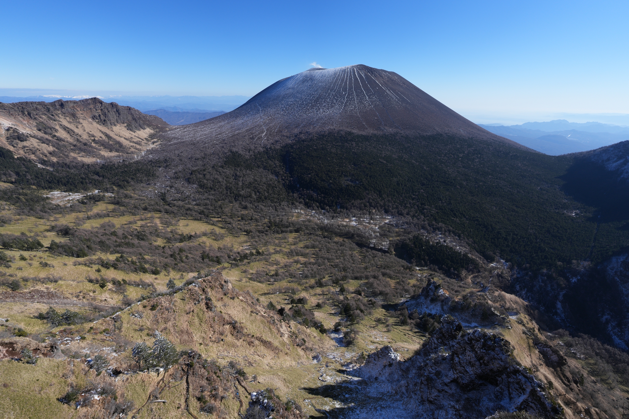 An ultra-wide photograph capturing a vast mountain landscape, with a large and beautiful mountain prominently featured behind the foreground mountain. Click to open modal