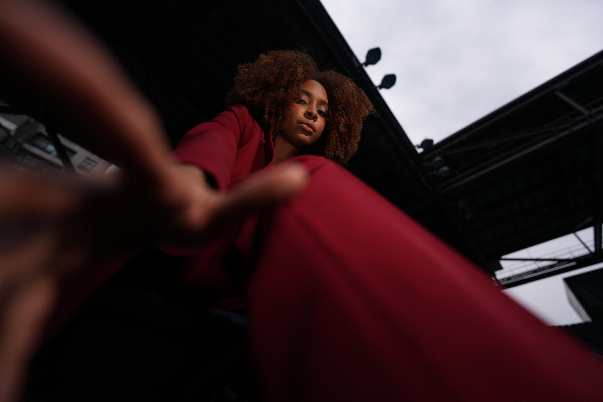 The composition is enhanced by capturing a woman in a red suit seated from a low angle, creating a sense of perspective. Her face appears small and central, while her hands are positioned close to the lens and it beautifully Bokeh. Click to open modal