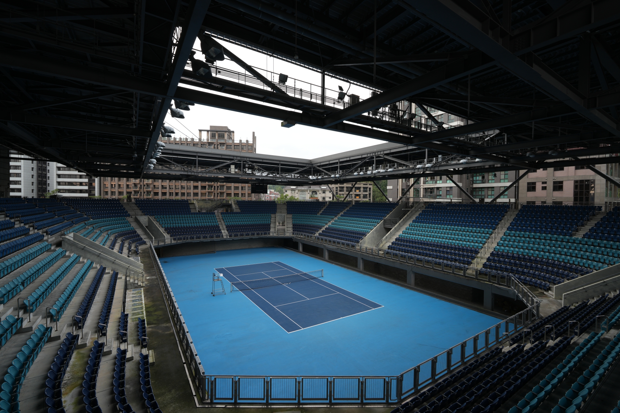 A photograph taken from above the seating area of a tennis arena, capturing the entire tennis court and seats in high resolution. Click to open modal