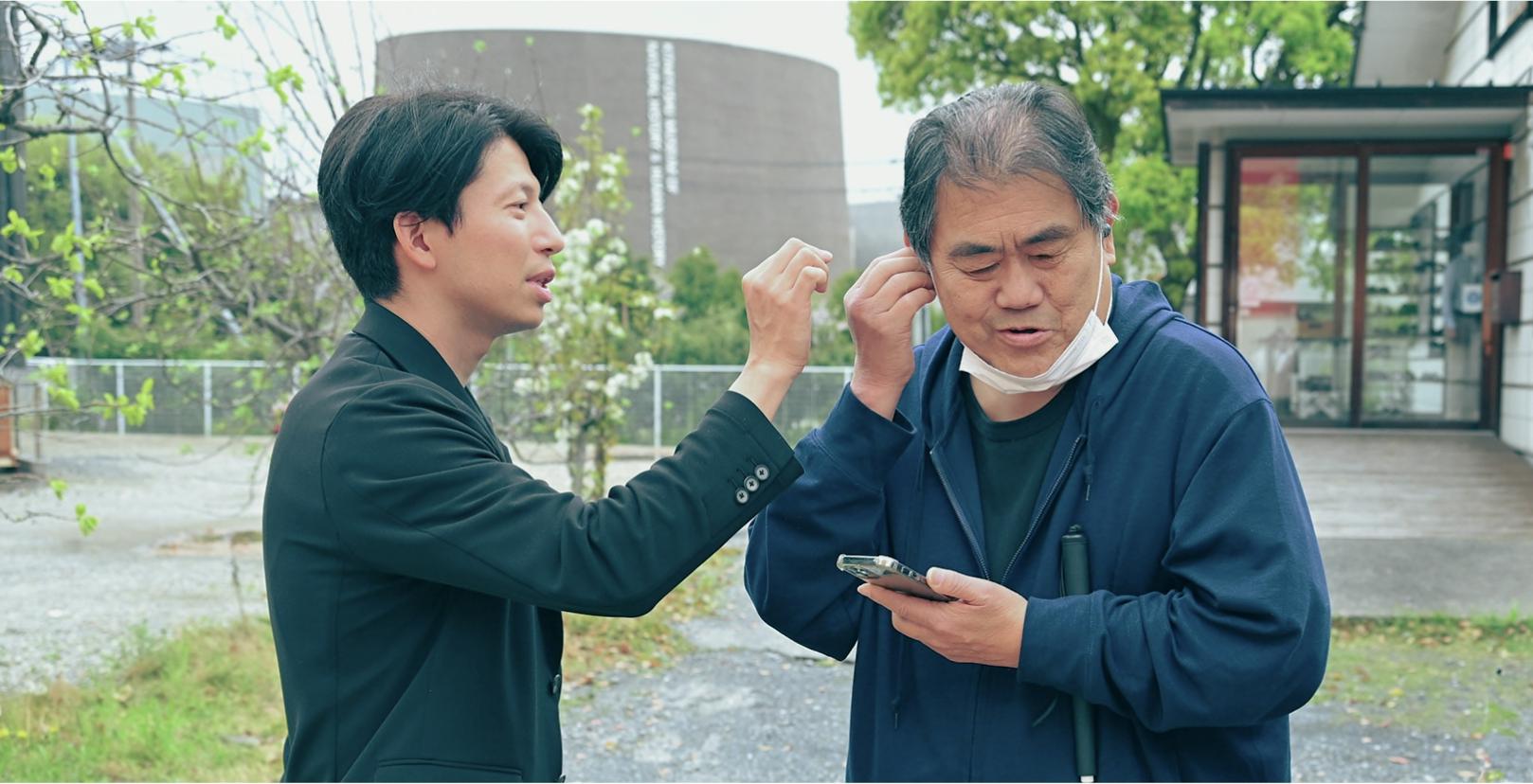 Shohei Takata is helping a male with visual impairments waring LinkBuds